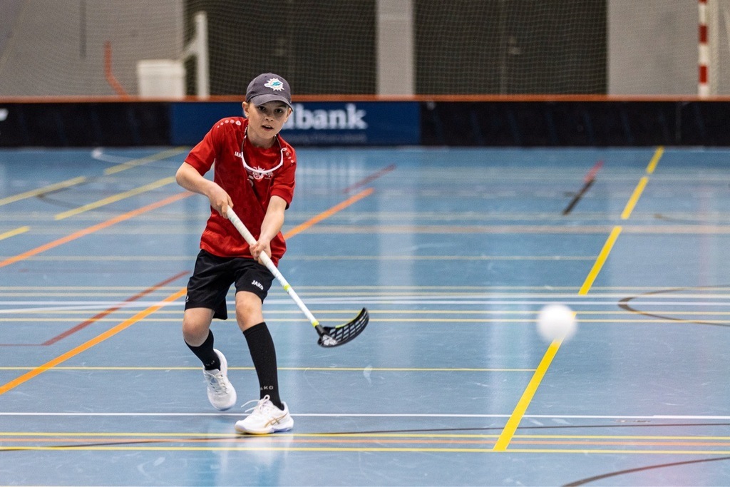 Ung floorballspiller fra Lystrup Vikings i rød trøje skyder bolden under træning i hallen